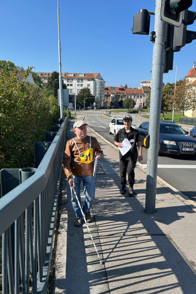 Soutěžící s andělem jde po chodníku a blíží se k semaforu